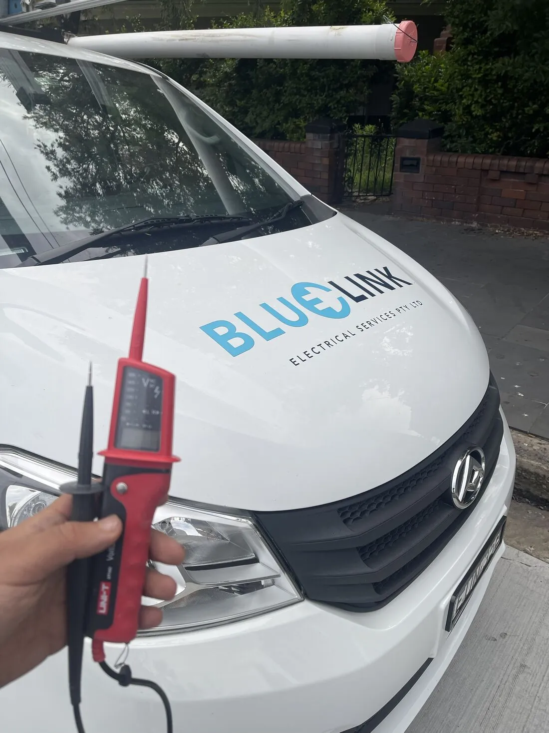 Electrician holding a voltage tester in front of the Blue Link van