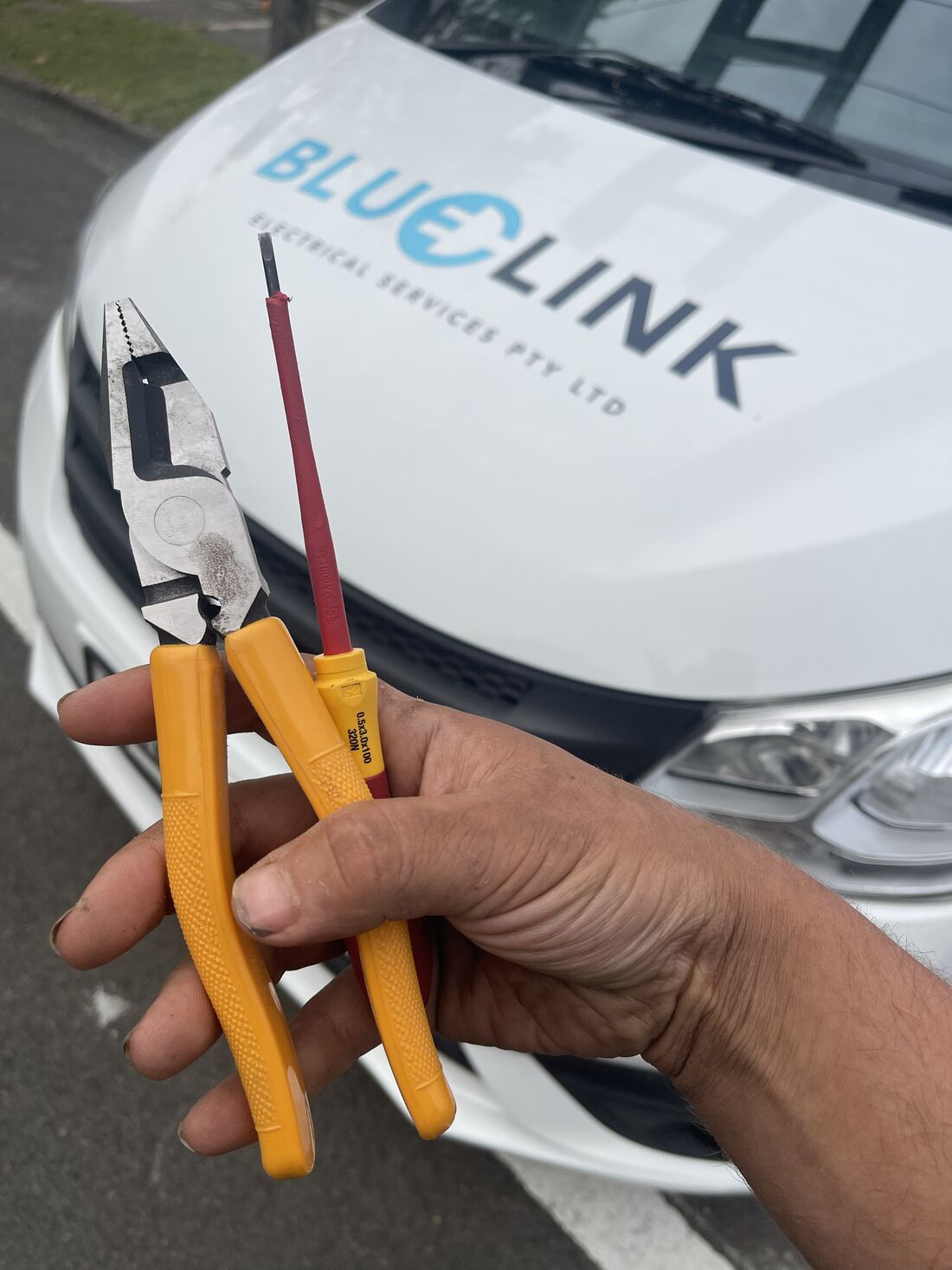 Insulated pliers and screwdriver in front of the Blue Link van
