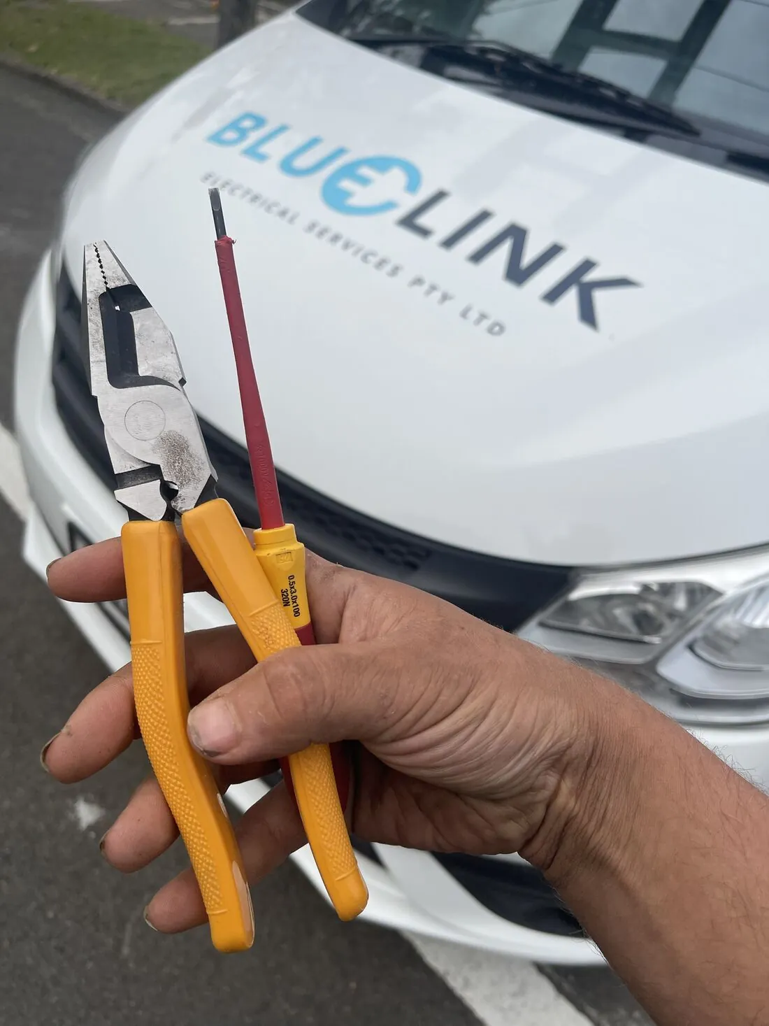 Insulated pliers and screwdriver in front of the Blue Link van