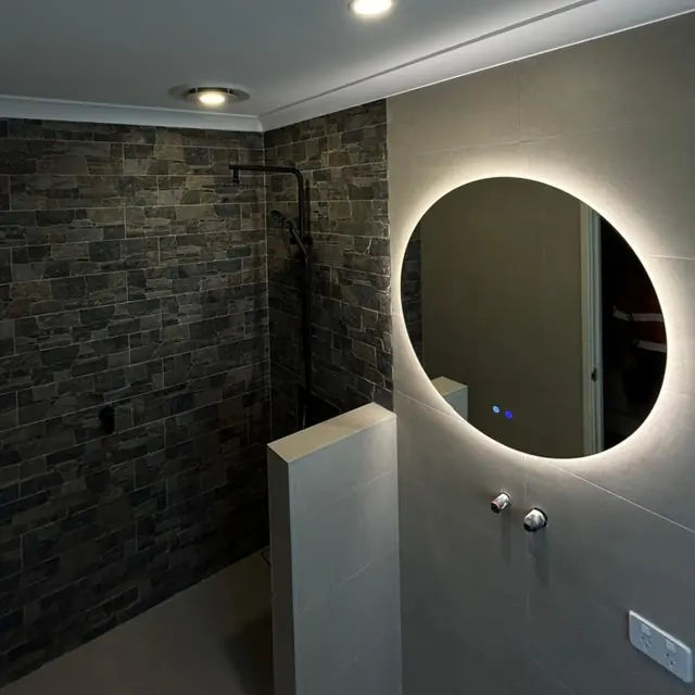 Round backlit LED mirror in a tiled bathroom with a ceiling light