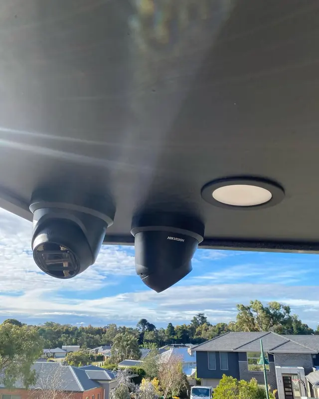 Two dome CCTV cameras mounted under an eave beside a downlight