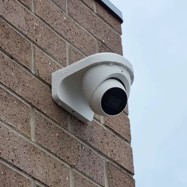 White turret CCTV camera on a mounting block on a brick wall