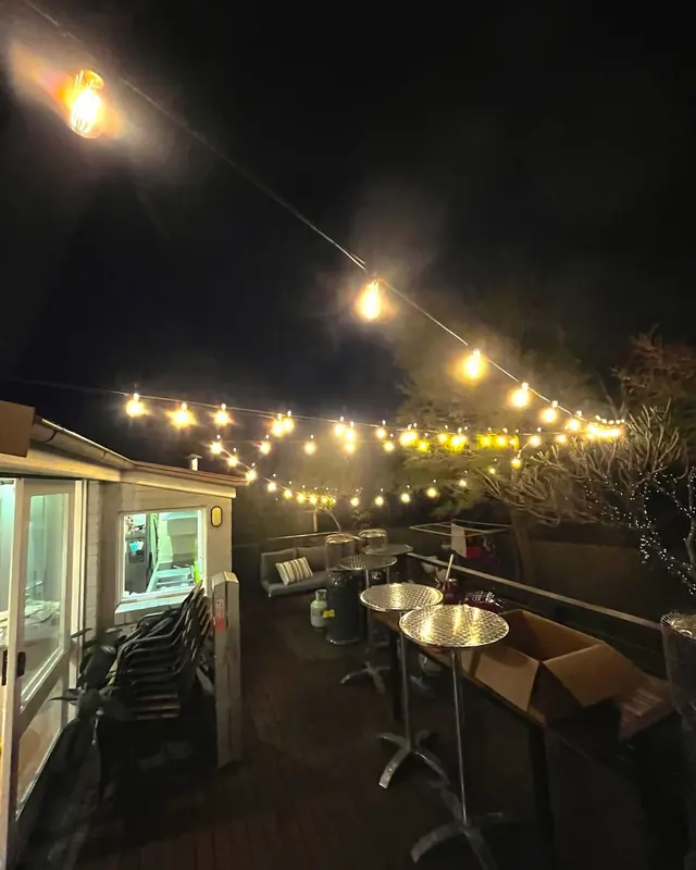 Festoon string lights above an outdoor deck with tables at night