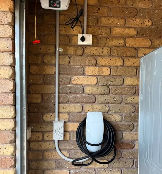 Wall-mounted EV charger on a brick garage wall with conduit and a power point