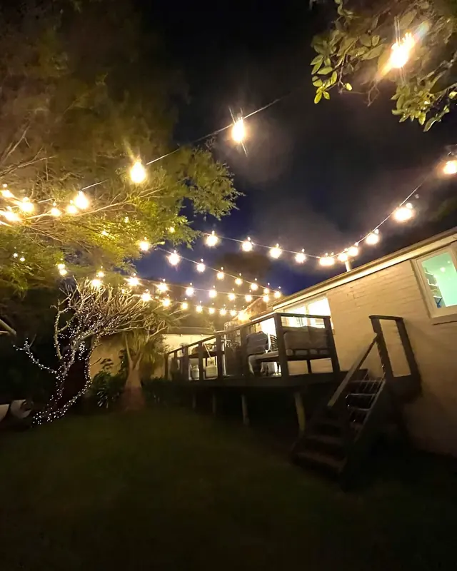 Festoon string lights across a backyard at night with a lit timber deck