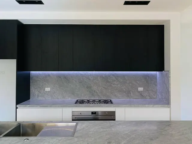LED strip lighting under black kitchen cabinets over a stone splashback