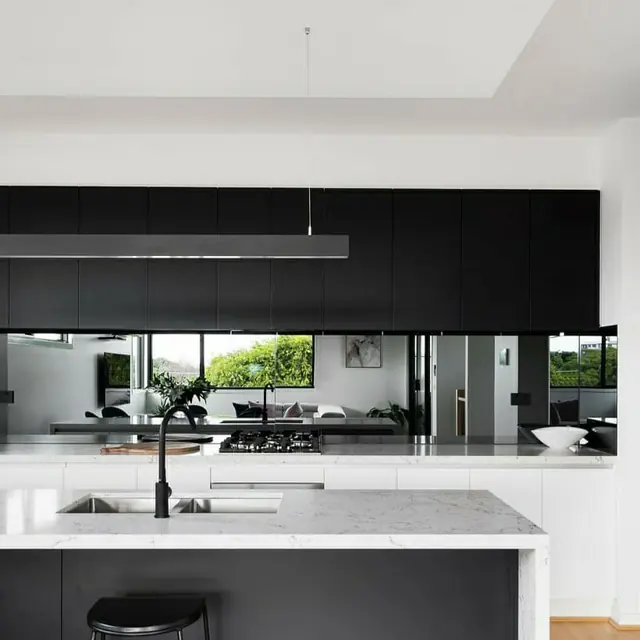 Linear pendant light above a marble kitchen island in a black and white kitchen
