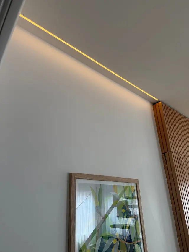 LED strip light recessed into a ceiling edge above a white wall