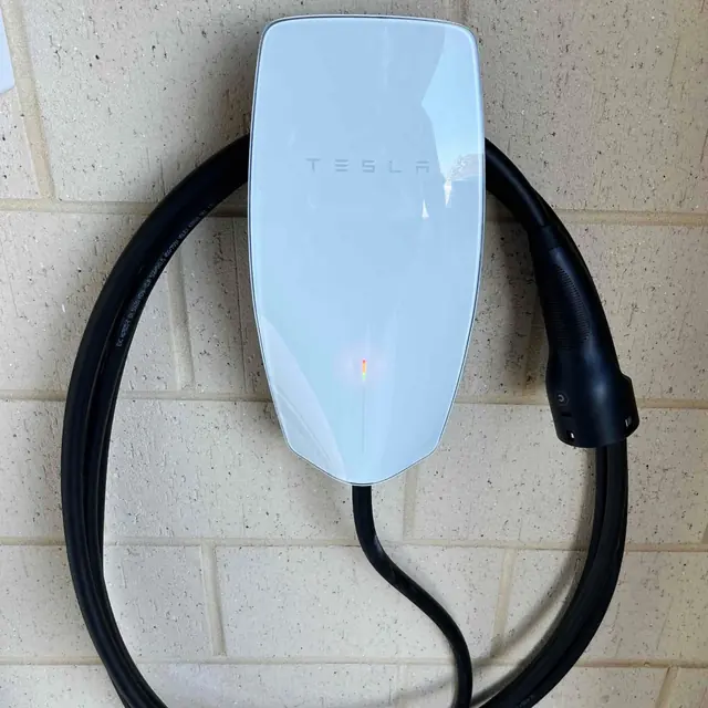 Tesla wall connector EV charger mounted on a painted brick wall
