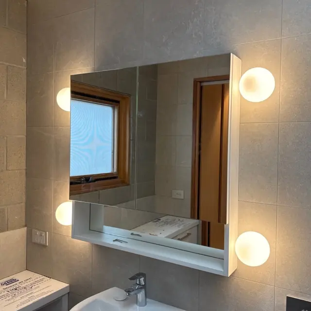 Mirror cabinet with globe wall lights either side in a tiled bathroom